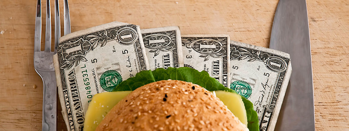 hamburger sitting on dollar bills with fork and knife