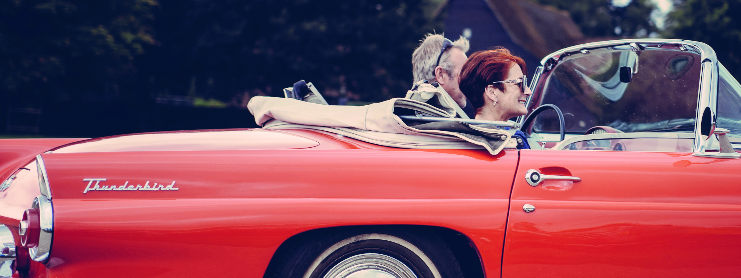 a middle aged couple riding in a convertible