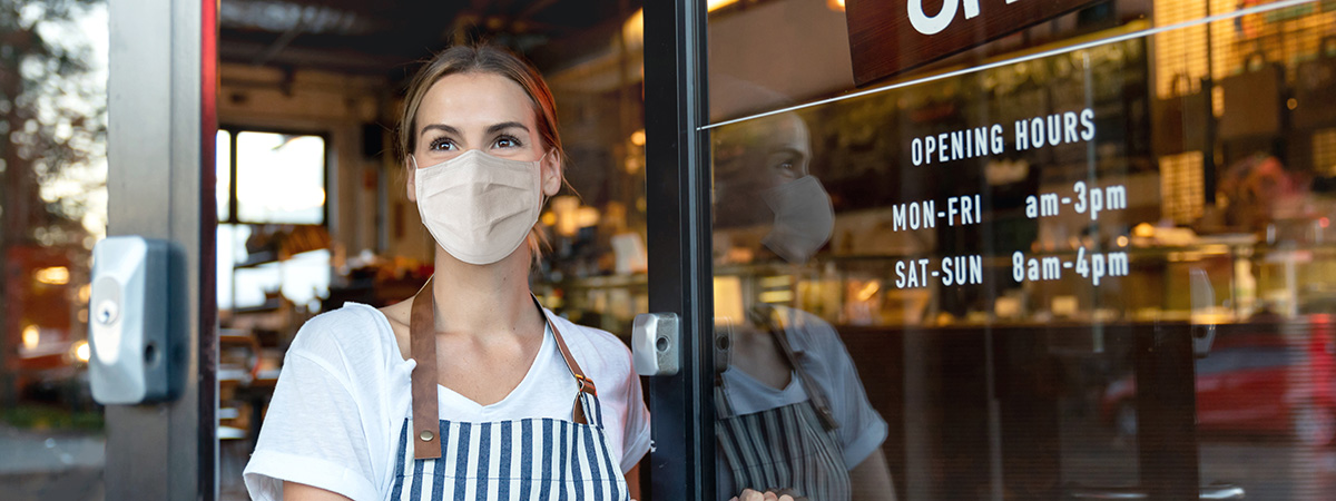 Business owner wearing mast at front door of business.