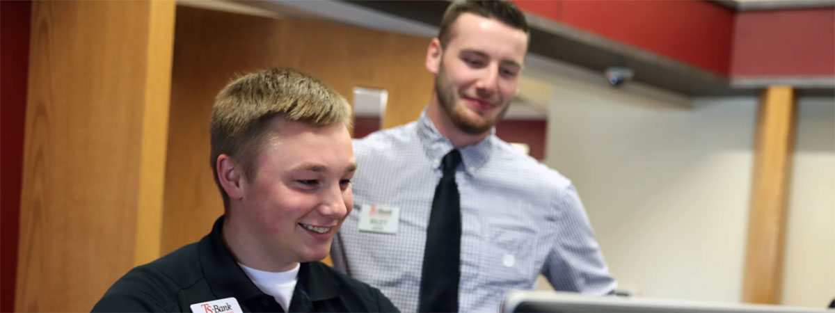 ts bank employee looks on as another works on a compute